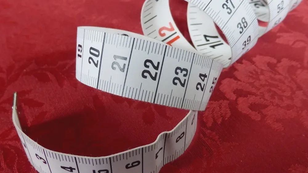 Mètre ruban de couture blanc déroulé sur une étoffe rouge damassée