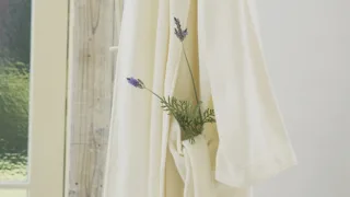 Peignoir de bain crème suspendu près d'une fenêtre, un brin de lavande glissé dans la poche
