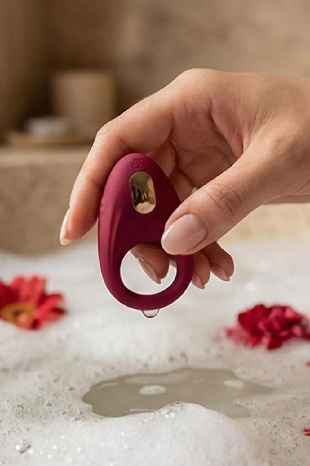 Anneau vibrant bordeaux tenu à la main au-dessus d'un bain moussant