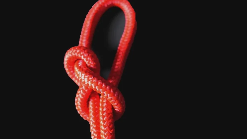 Nœud en huit noué dans une corde rouge tressée, sur fond noir
