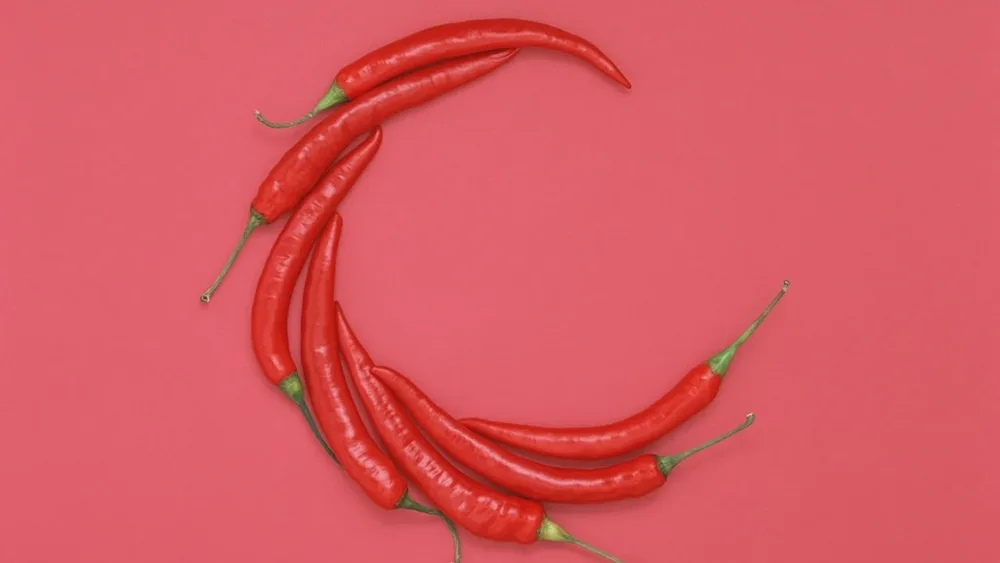 Piments rouges disposés en croissant sur un fond rose