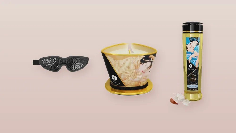 Masque bandeau noir, bougie de massage et huile de massage sur fond rose poudré