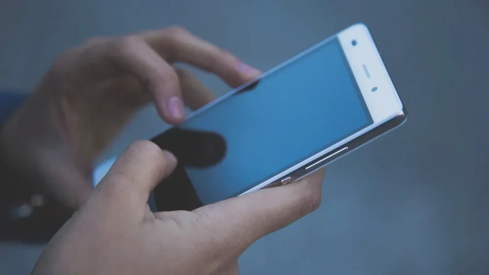 Deux mains tenant un smartphone blanc sur un fond bleu doux