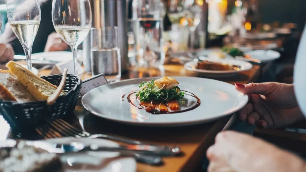 Assiette servie sur une table de dîner animée, verres de vin blanc et lumière chaude