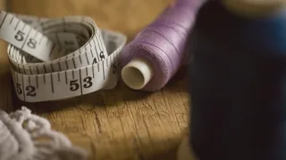 Mètre ruban de couturière, bobine de fil mauve et coton blanc crocheté posés sur une table en bois