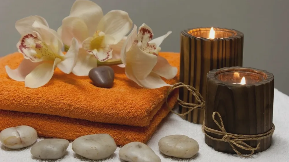 Serviettes orange, orchidées blanches, galets et bougies allumées dans une ambiance de massage