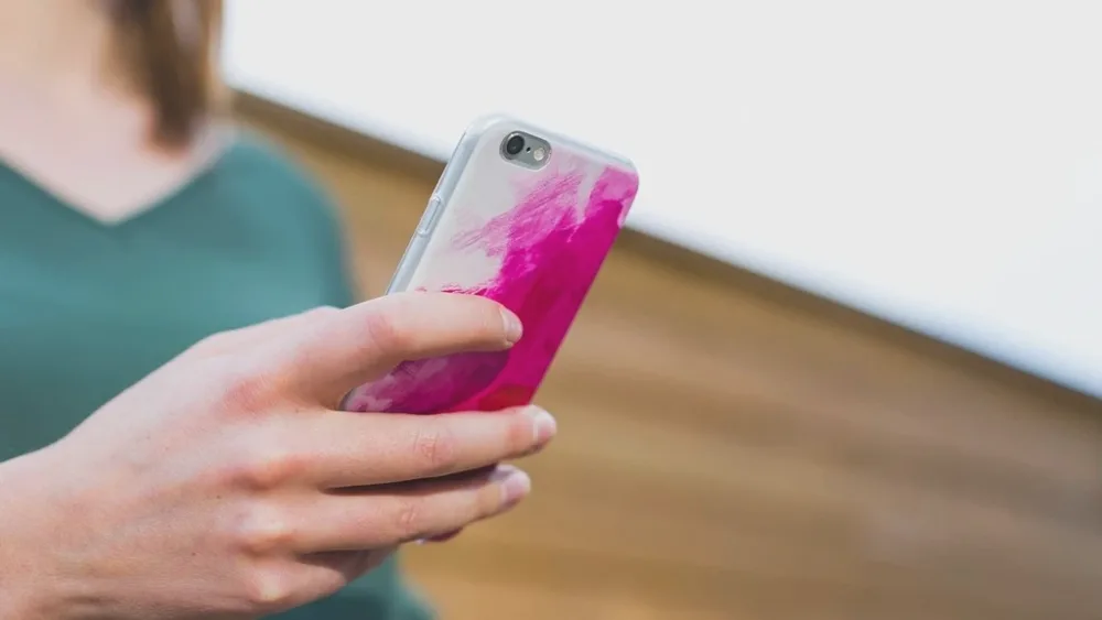 Main tenant un téléphone à coque rose fuchsia dans une lumière douce