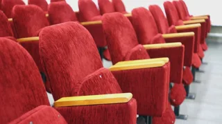 Rangées de fauteuils de théâtre en velours rouge, vides, dans une lumière claire