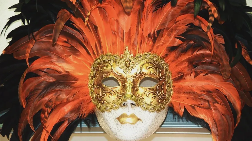 Masque vénitien doré entouré d'une couronne de plumes orange et noires