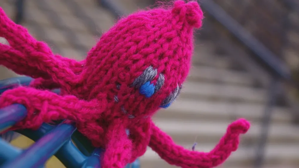 Pieuvre en tricot rose fuchsia aux longs tentacules, posée sur une rampe d'escalier