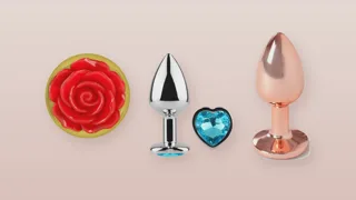 Trois bijoux anaux en métal sur fond rose poudré : base en rose rouge, strass bleu en forme de cœur et finition or rose