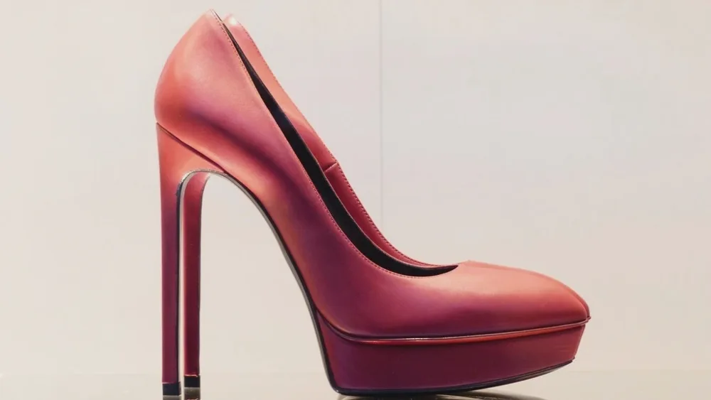 Escarpin à talon aiguille en cuir rouge posé seul sur une tablette, fond crème