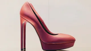 Escarpin à talon aiguille en cuir rouge posé seul sur une tablette, fond crème