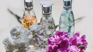 Trois flacons de parfum en verre derrière un bouquet d'œillets blancs et fuchsia