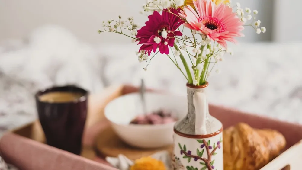 Plateau de petit-déjeuner au lit avec café, croissant et bouquet de gerberas roses