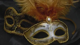 Deux loups de carnaval dorés, l'un orné de plumes, posés sur un tissu sombre