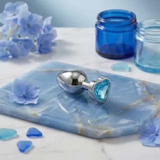 Plug anal en silicone posé sur un tissu clair à côté d'un flacon de lubrifiant