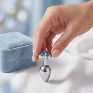 Plug anal bijou en métal avec base ornée d'un cristal, posé sur un tissu clair