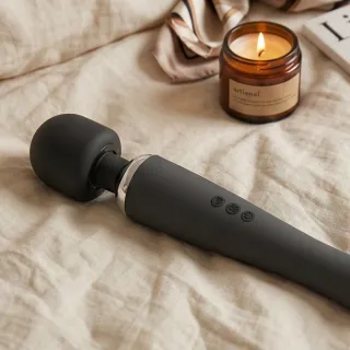 Vibromasseur baguette magique au long manche et à la grosse tête arrondie posé sur un tissu clair