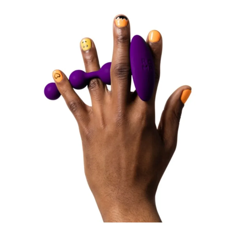 Perles anales en silicone violet avec trois billes de tailles croissantes, présentées sur une main, les billes marquées de symboles emoji souriants