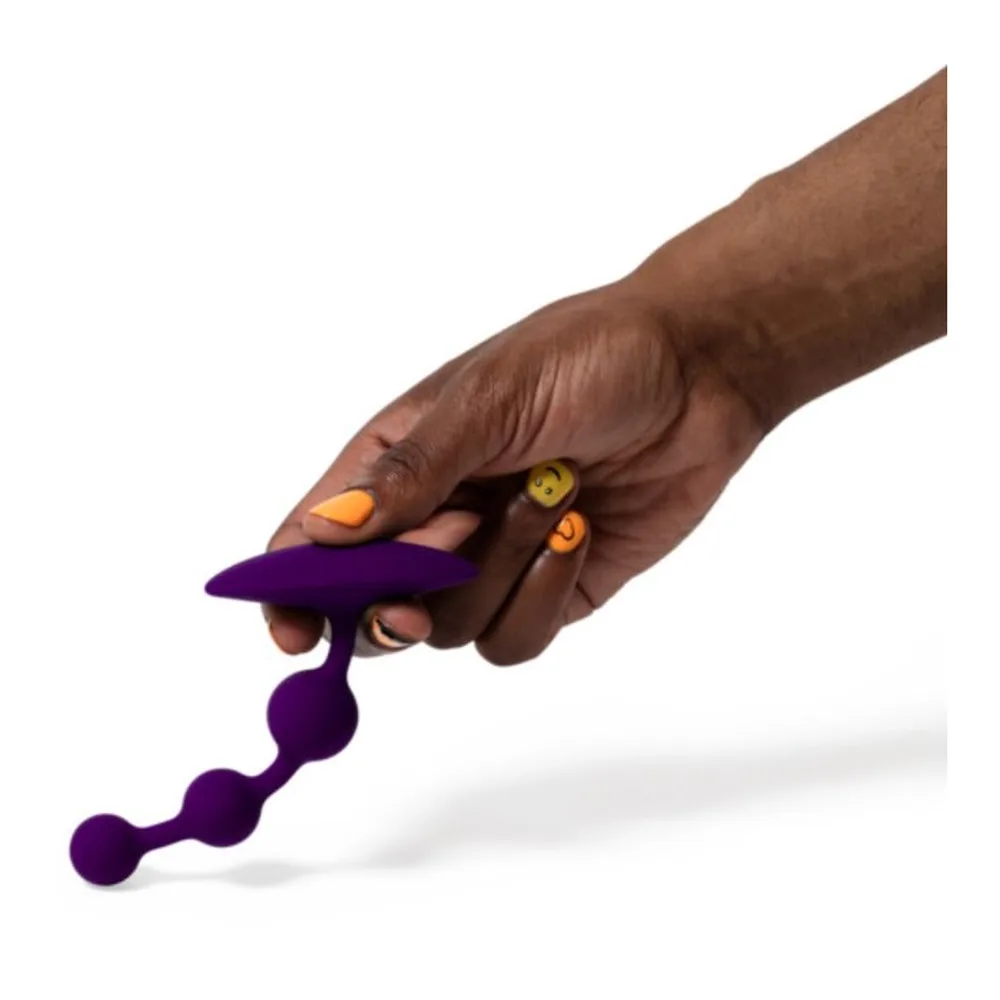 Perles anales en silicone violet avec trois billes de tailles croissantes, présentées sur une main, les billes marquées de symboles emoji souriants
