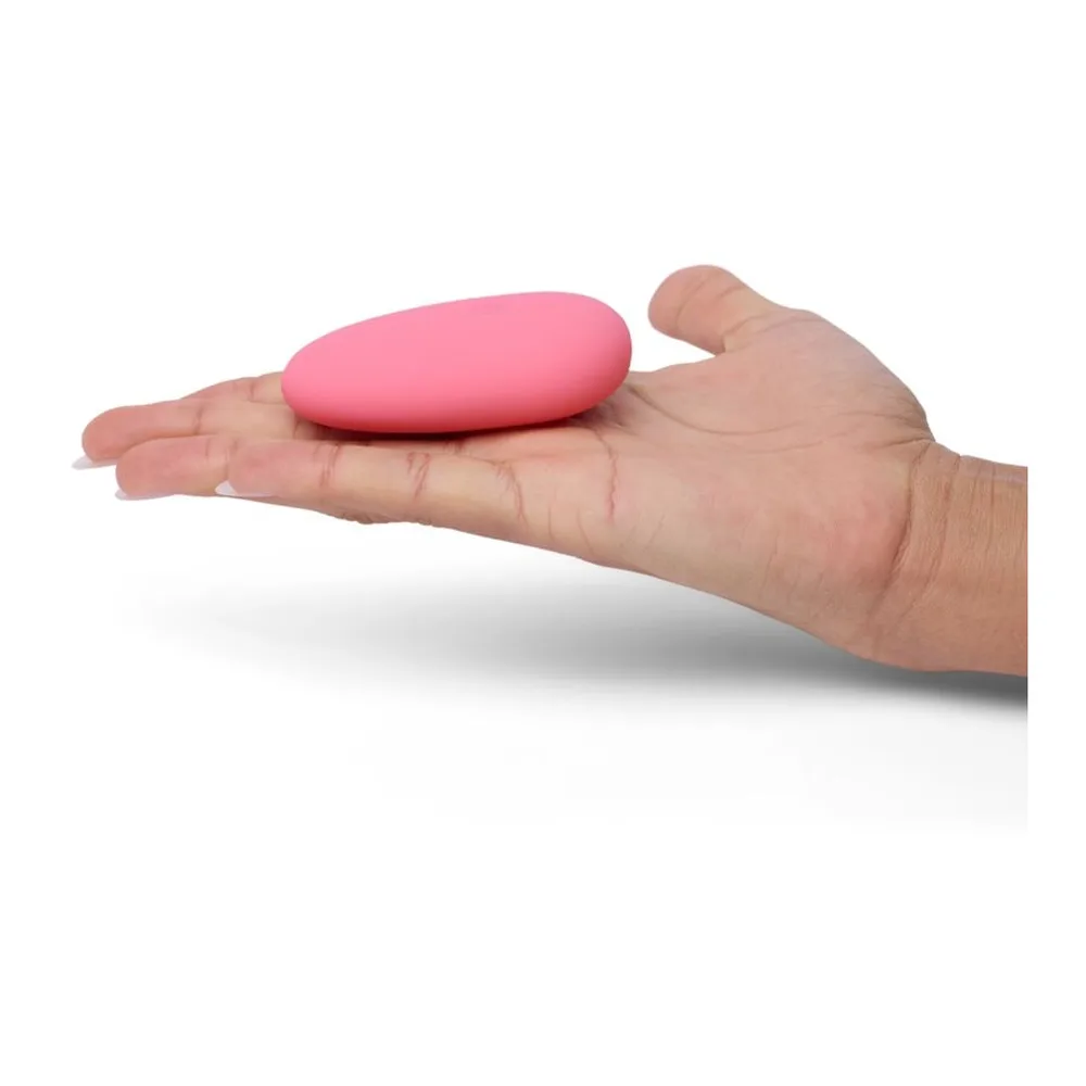 Stimulateur clitoridien rose en forme de galet lisse et plat, aux bords arrondis, avec un petit bouton de commande visible sur le côté