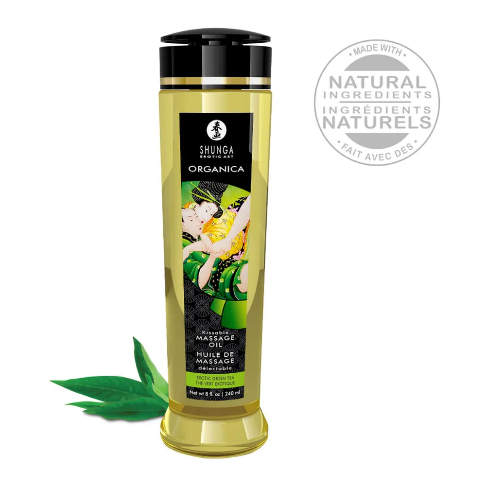 Flacon transparent rempli d'huile jaune pâle Shunga Organica au thé vert, étiquette noire et dorée, entouré de feuilles de thé vert frais