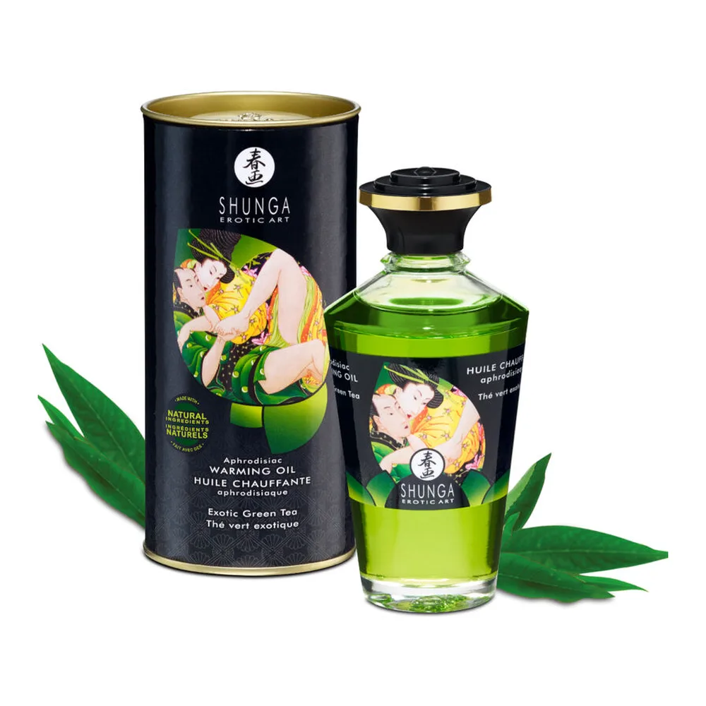 Huile de massage chauffante Shunga au thé vert bio en flacon vert clair avec bouchon doré, présentée avec son emballage cylindrique noir et doré orné d'illustration inspirée d'art érotique, entouré de feuilles vertes
