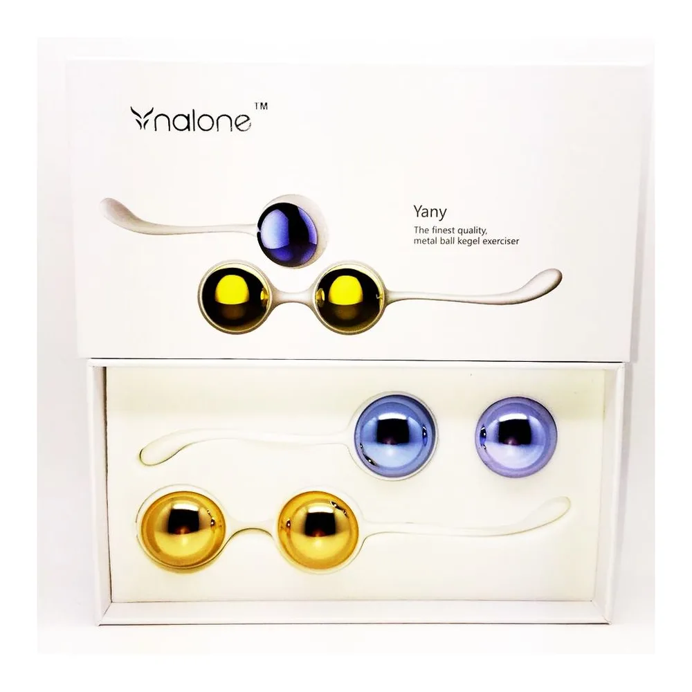 Coffret Yany Nalone contenant quatre boules de geisha en métal lisse aux teintes or et bleu, montées sur tiges courbes, et deux billes isolées bleu pervenche, présenté ouvert sur fond blanc