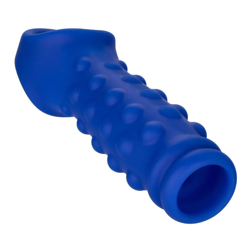 Gaine en silicone bleu avec picots texturés sur toute la surface, embout transparent et sangle scrotale intégrée blanche, vue en angle sur fond blanc