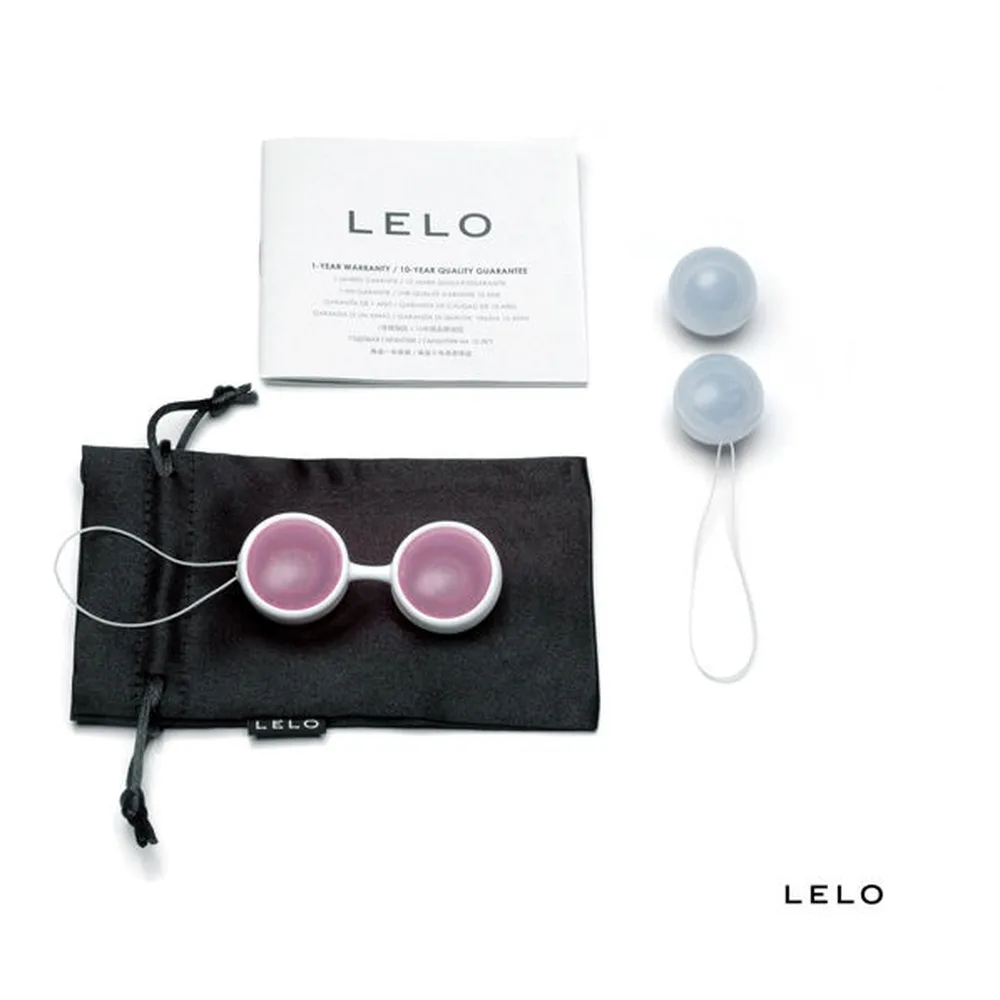 Deux boules de Geisha en silicone, l'une grise et l'une rose, tenues dans une main avec leurs anneaux de suspension blancs visibles, sur fond blanc