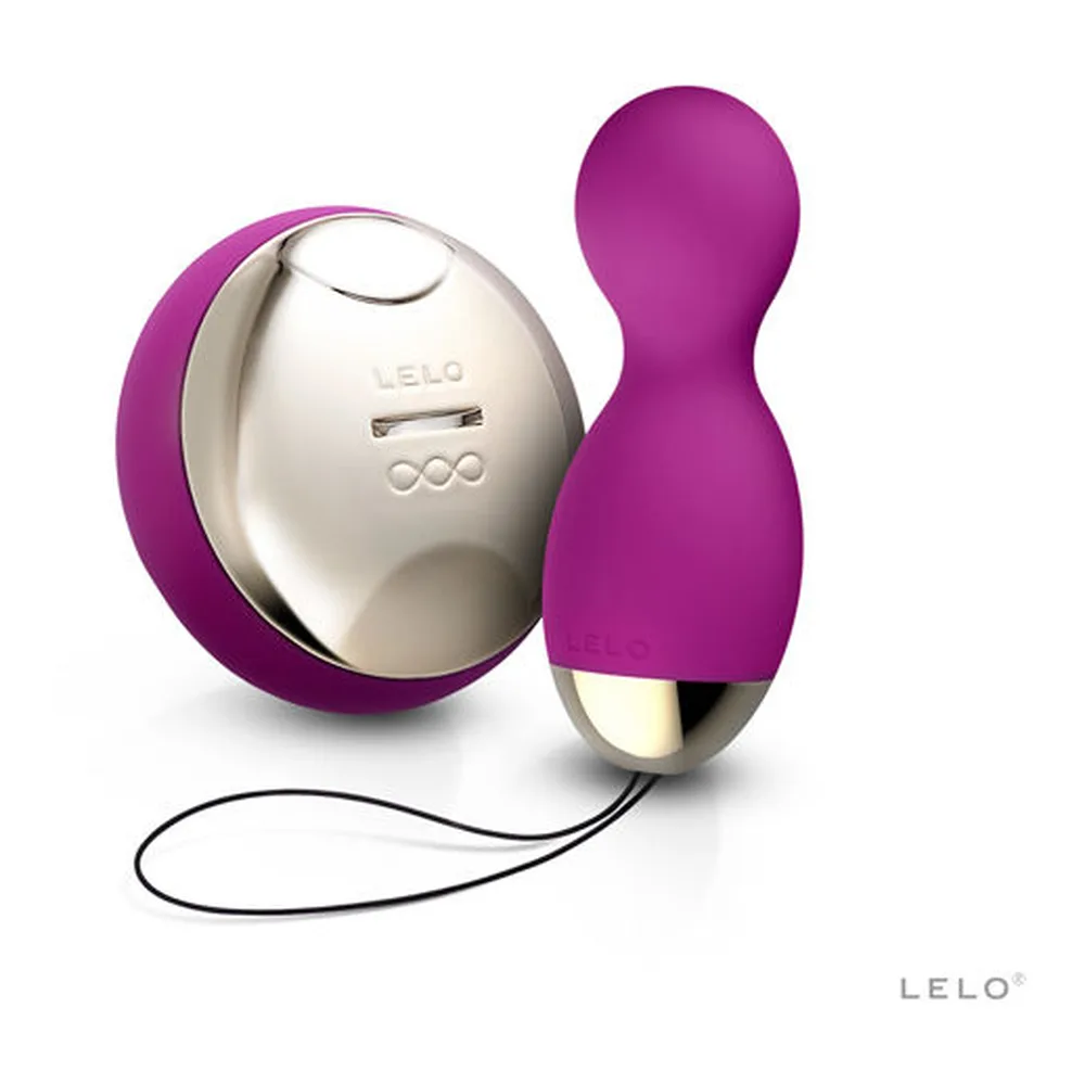 Boule de Geisha Hula Beads en silicone magenta avec détails en métal argenté, télécommande sans fil et cordon d'attache, présentées avec leur rangement blanc crème de marque LELO