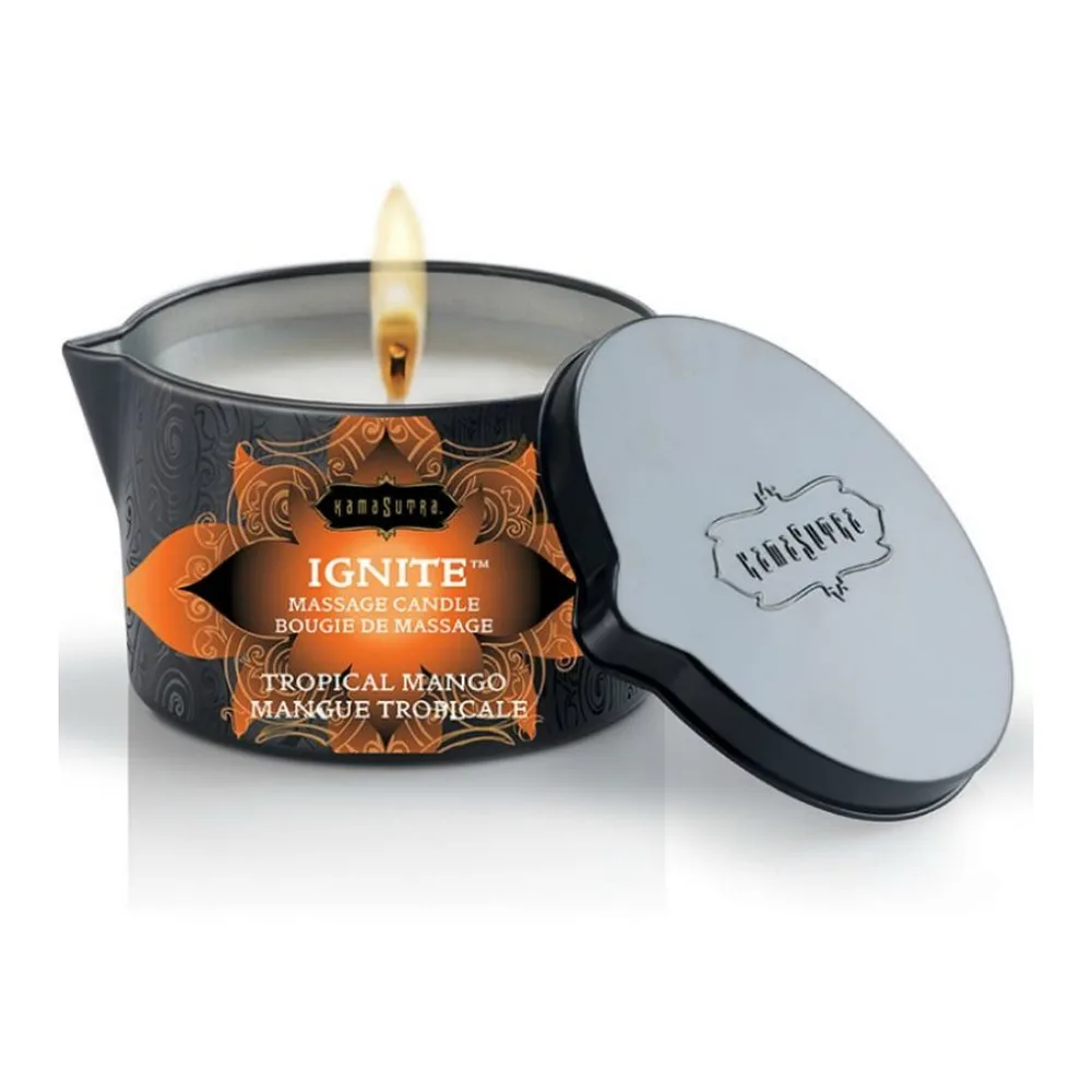 Bougie de massage noire avec étiquette orange Tropical Mango, allumée avec une mèche dorée, accompagnée de son couvercle gris et sa cuillère applicatrice