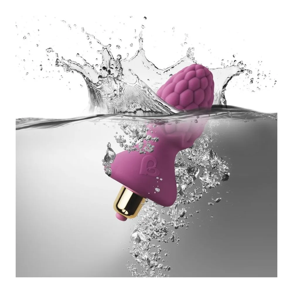 Plug anal en silicone rose magenta en forme de framboise avec texture grainée, tenu en main sur fond blanc, module vibrant visible en base
