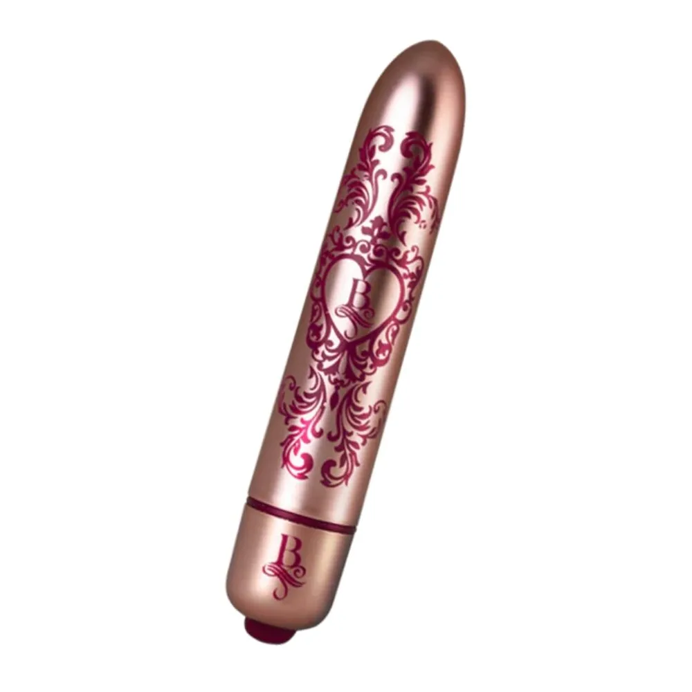 Stimulateur clitoridien de forme allongée en silicone couleur rose métallisé, orné de motifs floraux damassés en rose foncé, avec anneau de commande à la base, sur fond blanc