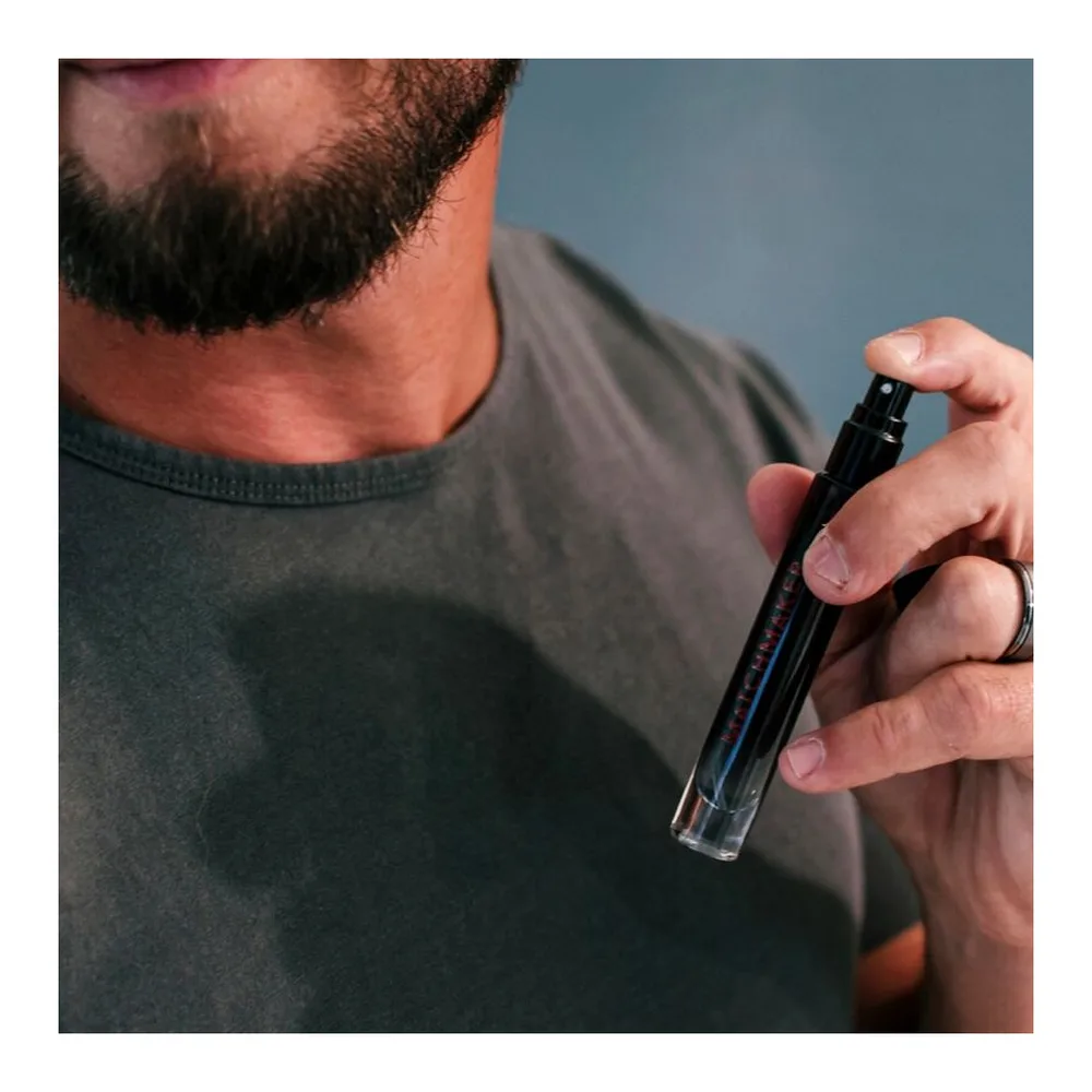 Flacon vaporisateur en verre teinté de parfum aux phéromones Matchmaker, 10 ml, à côté de son étui cylindrique noir et rouge, avec bouchon pulvérisateur noir