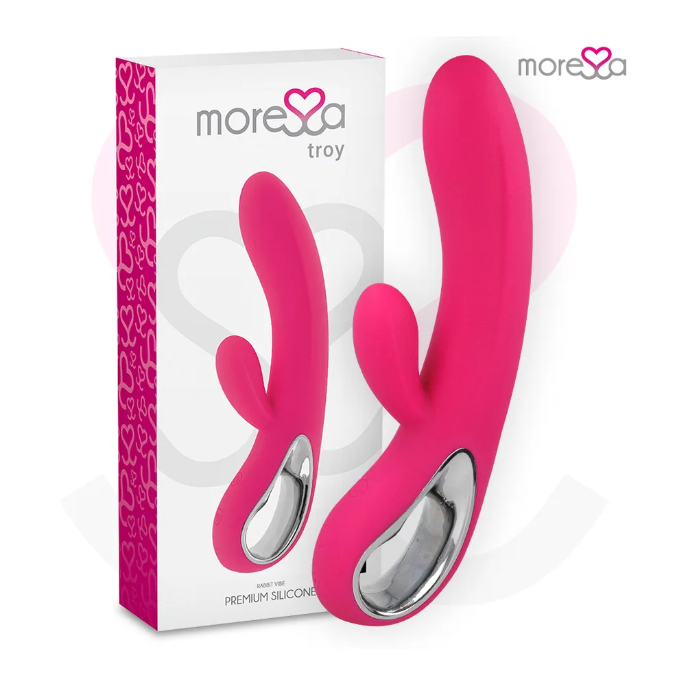 Vibromasseur rabbit en silicone rose vif tenu en main, avec bran principal courbe et petit bras latéral, sur fond blanc avec cœur rose pâle et logo de marque