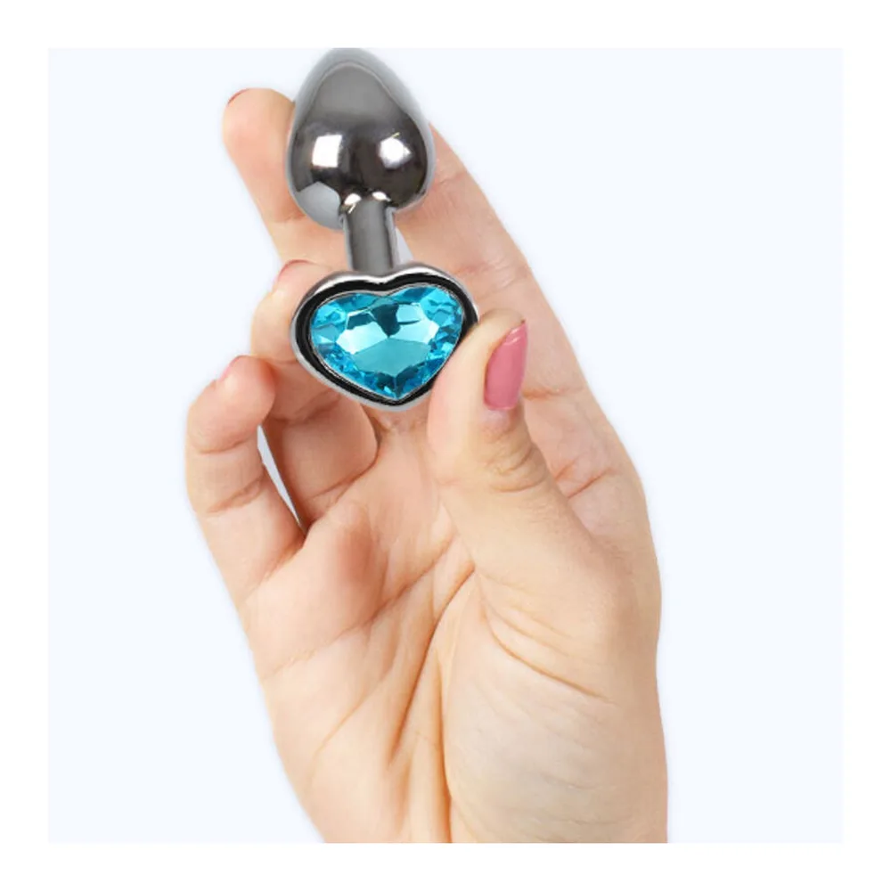 Plug anal en aluminium poli gris tenu en main, orné d'un strass bleu taillé en forme de cœur à sa base
