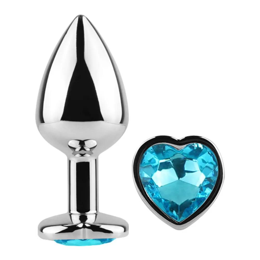Plug anal en aluminium poli gris tenu en main, orné d'un strass bleu taillé en forme de cœur à sa base