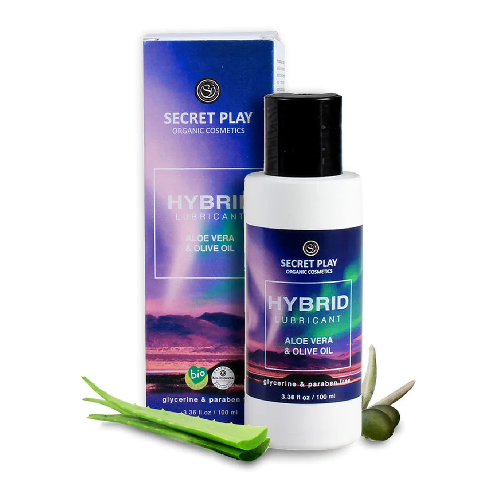 Flacon blanc de lubrifiant hybride Secret Play avec bouchon noir, accompagné de son emballage bleu dégradé rose, feuilles d'aloe vera et olive fraîches