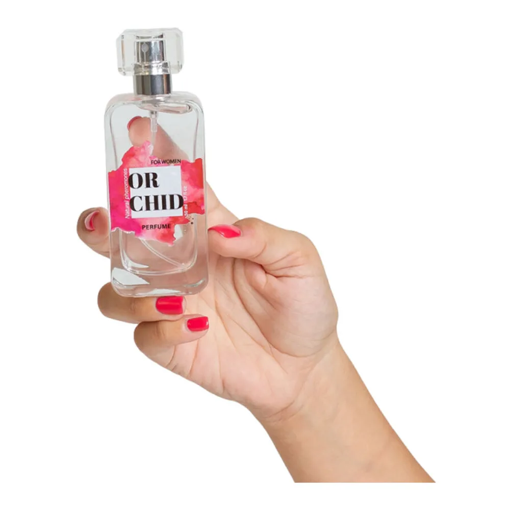 Flacon de parfum aux phéromones tenu en main, verre transparent avec étiquette rose vif, bouchon chrome, spray visible, notes d'orchidée noire et vanille