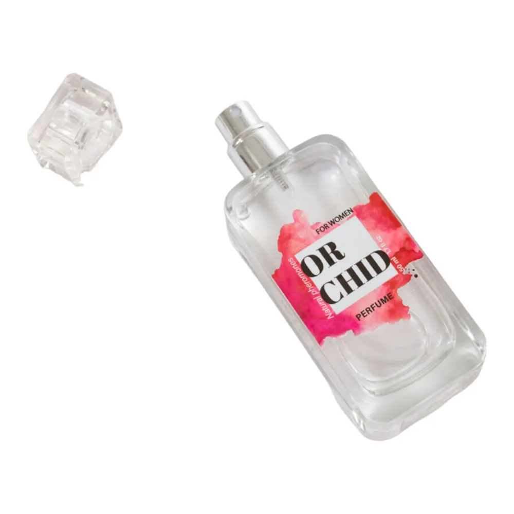 Flacon de parfum aux phéromones tenu en main, verre transparent avec étiquette rose vif, bouchon chrome, spray visible, notes d'orchidée noire et vanille