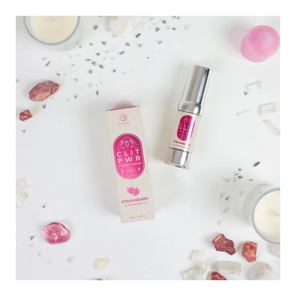 Baume clitoris rose bonbon à la fraise en tube airless argenté, présenté en main face à son emballage rose et beige de forme hexagonale, sur fond blanc
