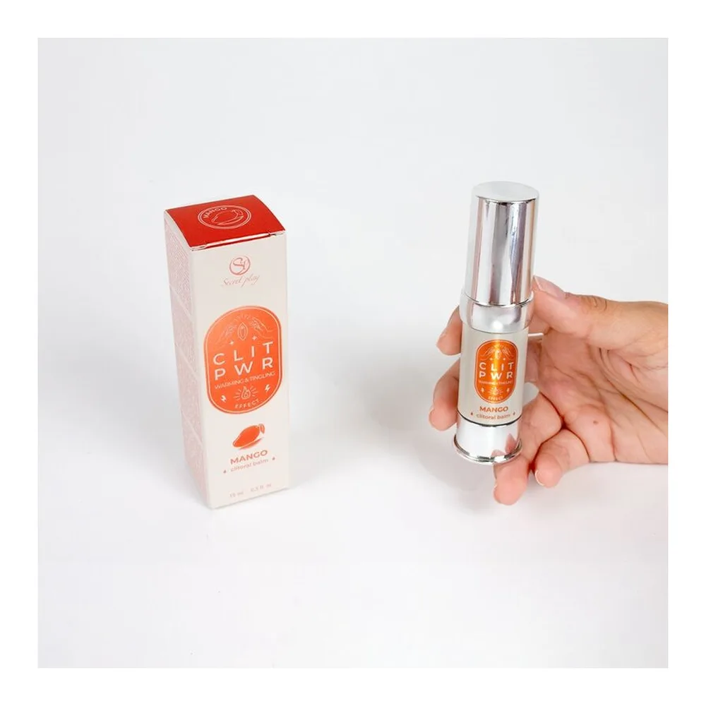 Baume clitoridien Clit Pwr en tube blanc et flacon applicateur à bille, entouré de cristaux d'ambre, de lait et de mangue sur fond blanc