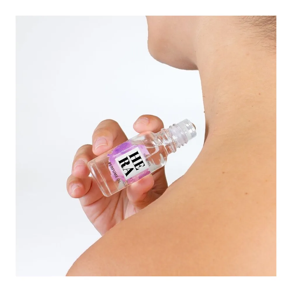 Boîte violette et blanche du parfum Hera avec flacon roll-on transparent contenant une huile parfumée incolore, bouchon noir, présenté sur socle blanc avec emballage