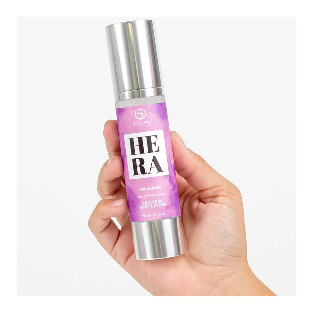 Flacon de lotion corporelle Hera Silk Lotion en spray avec capuchon argenté, étiquette rose vif, tenu en main sur fond blanc
