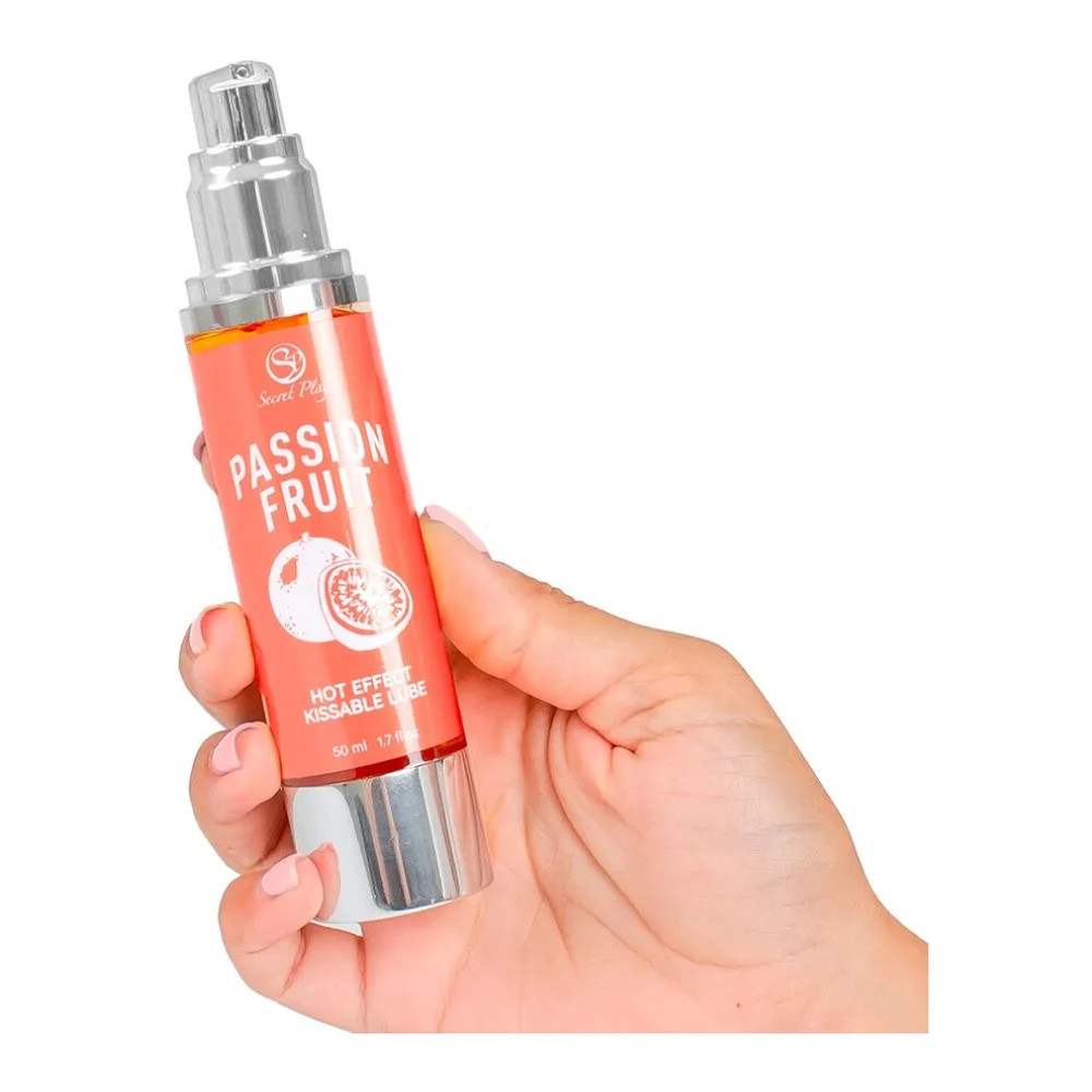 Flacon airless rouge corail de 50 ml de lubrifiant chauffant au fruit de la passion, tenu en main, avec bouchon et pompe spray en métal chromé