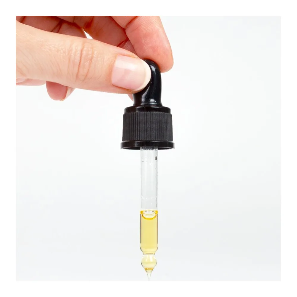 Pipette compte-gouttes avec capuchon noir tenue par une main, contenant un sérum huileux jaune clair sur fond blanc