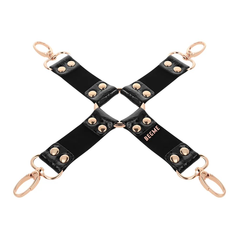 Croix de liaison en cuir noir vegan avec quatre mousquetons rose doré, ornée de clous métalliques, vue sur fond blanc