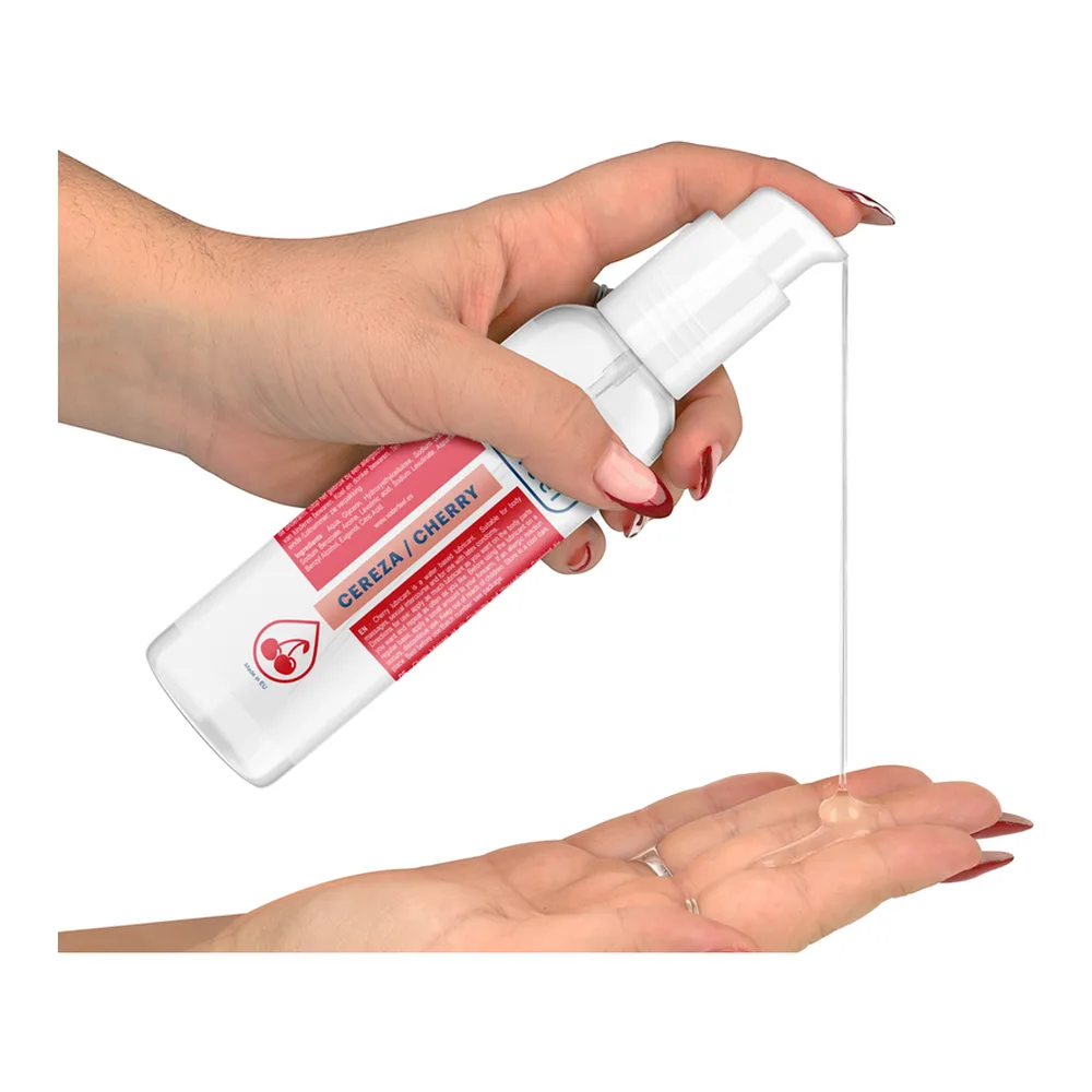 Flacon blanc de lubrifiant aromatisé cerise avec bouchon pompe, entouré d'éclaboussures d'eau rouge et de cerises fraîches sur fond blanc